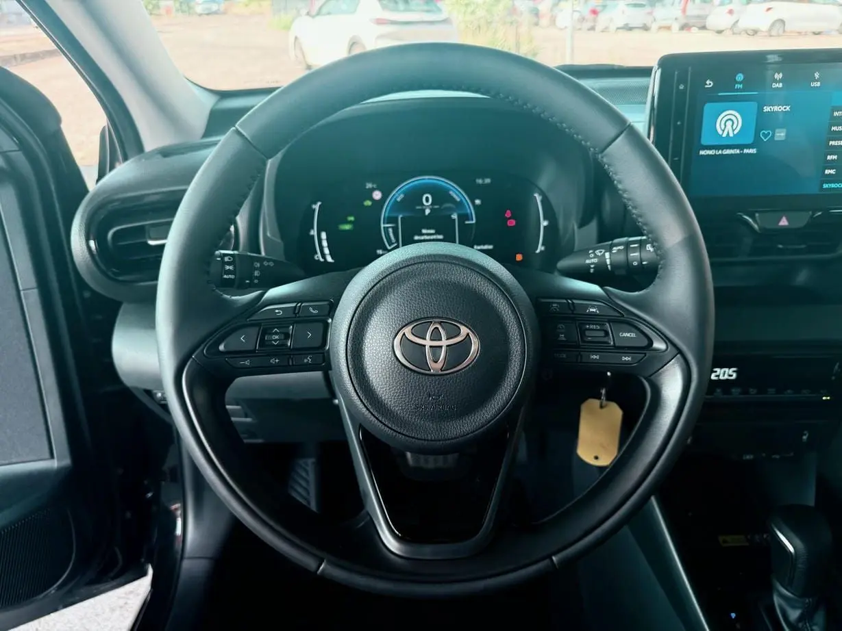 Vue rapprochée du volant noir de la Toyota Yaris Hybrid 2025 avec tableau de bord numérique et écran tactile central.