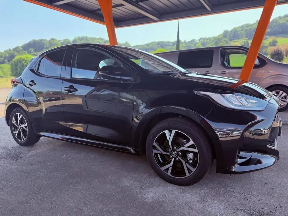 Toyota Yaris hybride noire vue de profil côté gauche sous abri avec jantes alliage et phares LED distinctifs.