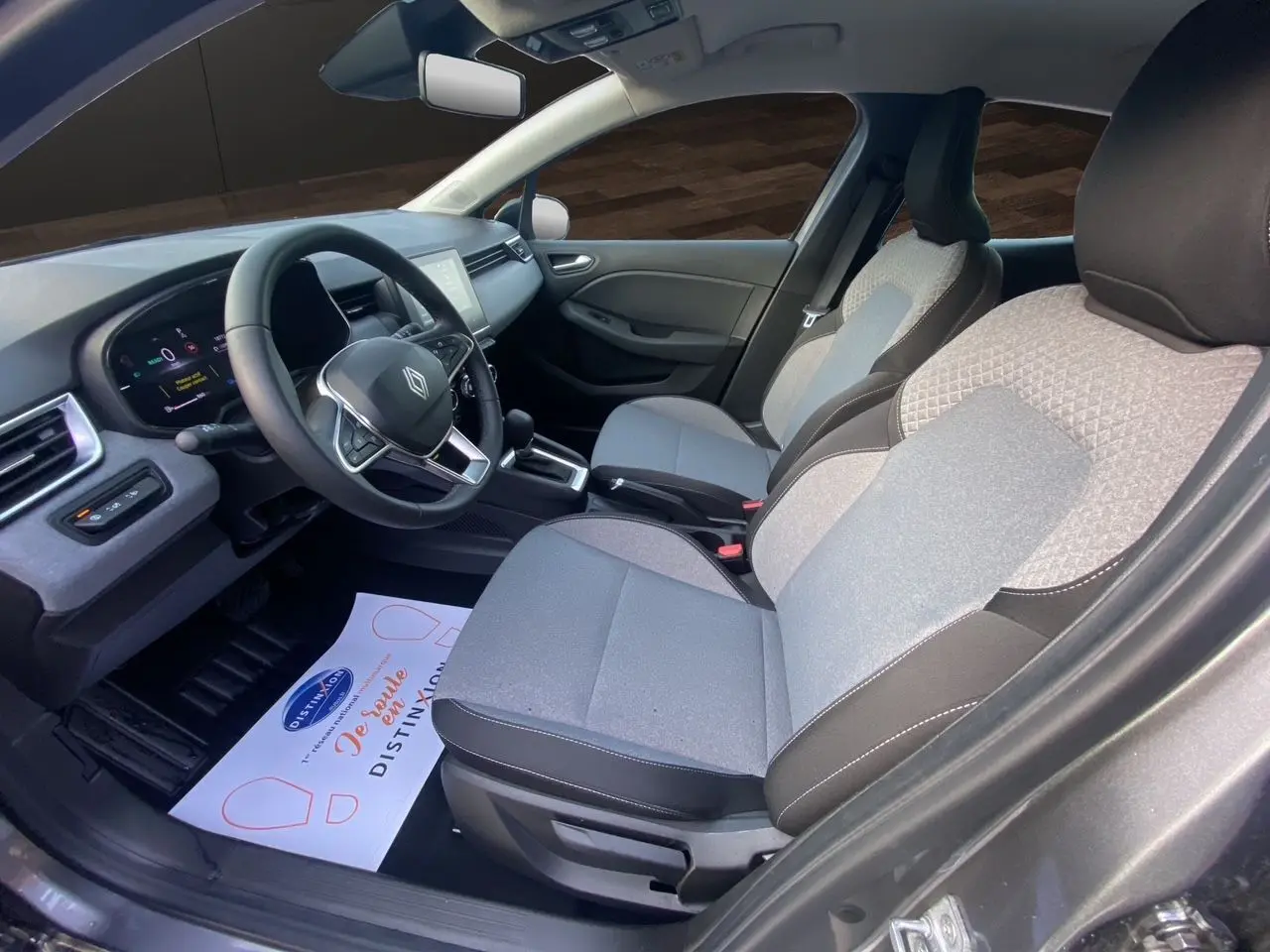 Vue intérieure côté conducteur de la Renault Clio V E-Tech gris schiste, avec sellerie textile gris à motif 3D et tableau de bord moderne.