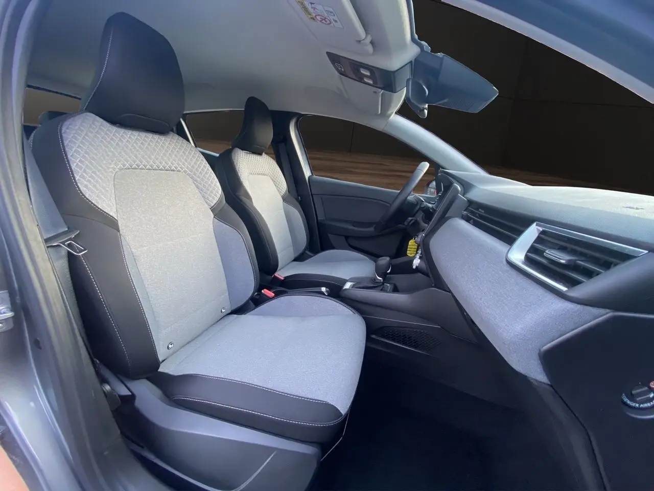 Vue intérieure côté gauche de la Renault Clio V E-Tech gris schiste, montrant les sièges avant en tissu gris à motif 3D.