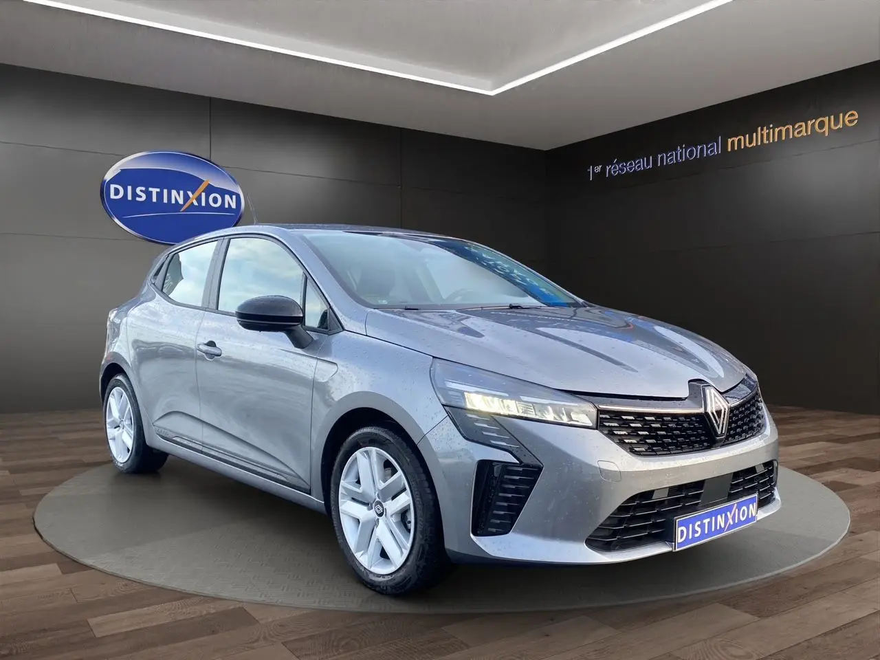 Renault Clio V E-Tech gris schiste vue 3/4 avant, avec projecteurs LED allumés et jantes alliage blanches.