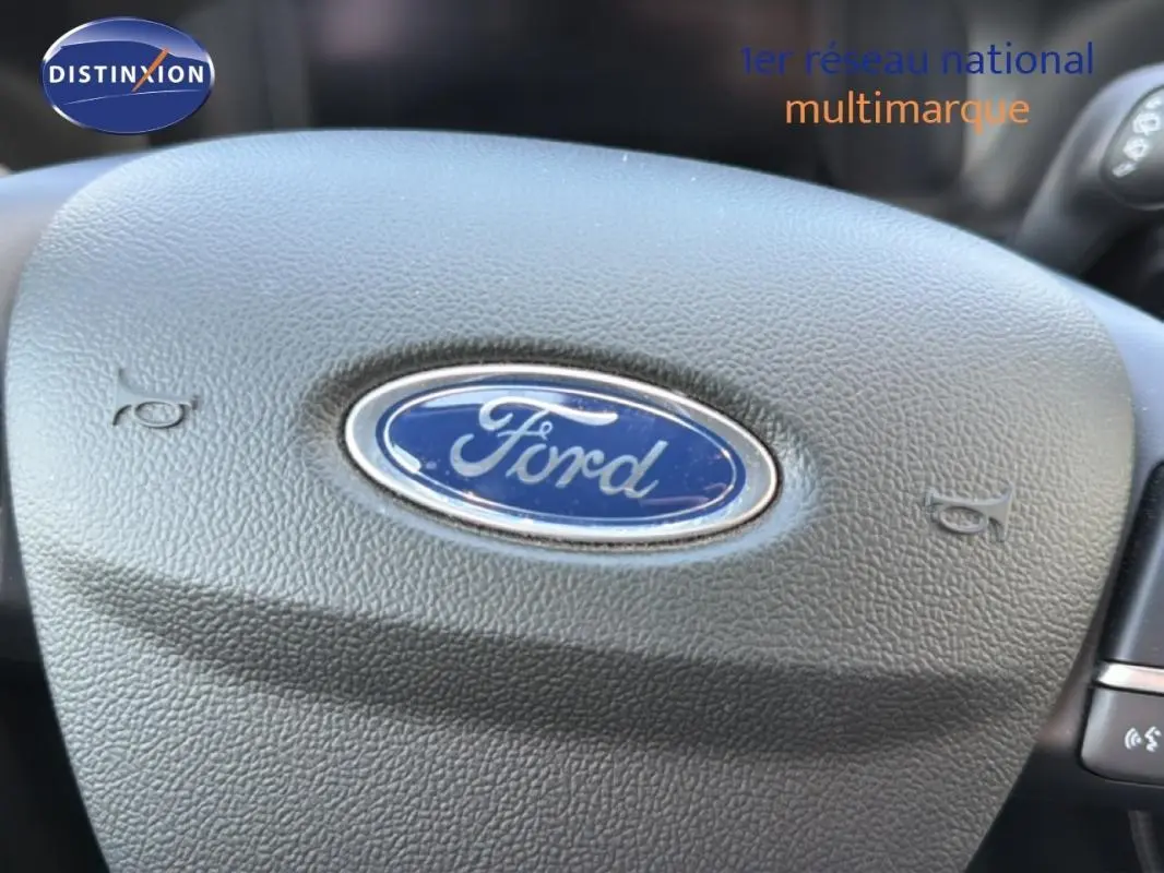 Gros plan sur le volant noir avec logo Ford au centre, intérieur du Ford Kuga 2024 visible en arrière-plan.