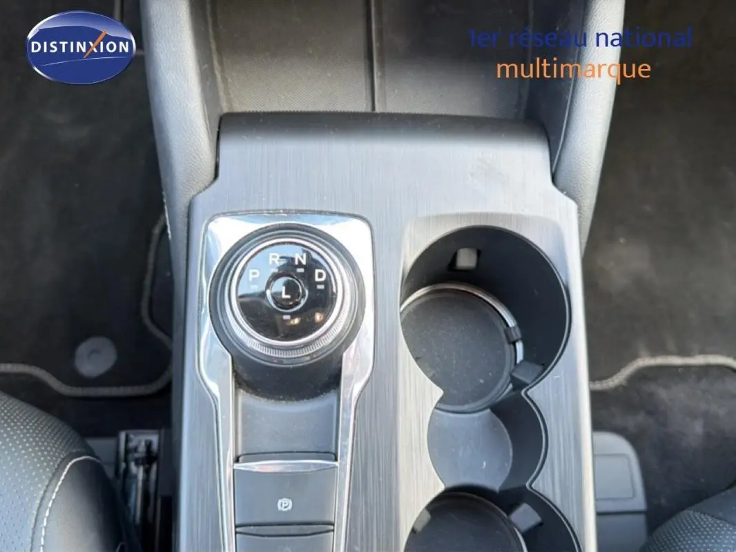 Vue plongeante sur la console centrale noire du Ford Kuga 2024 avec sélecteur rotatif de boîte auto et porte-gobelets.