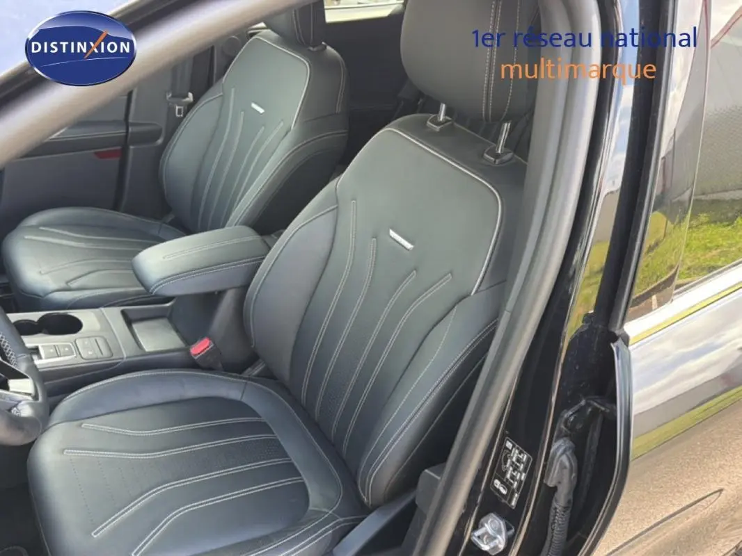 Vue intérieure côté conducteur du Ford Kuga noir 2024, sièges sport en cuir avec accoudoir central et coutures apparentes.
