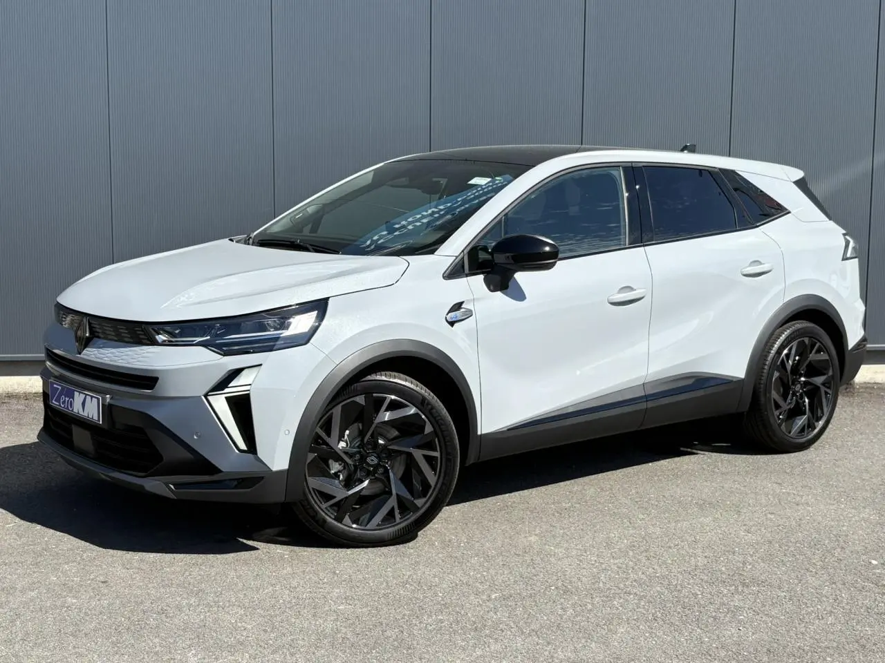 Renault Symbioz 2025 blanc vue 3/4 avant avec toit noir, jantes noires et détails modernes sur fond urbain.