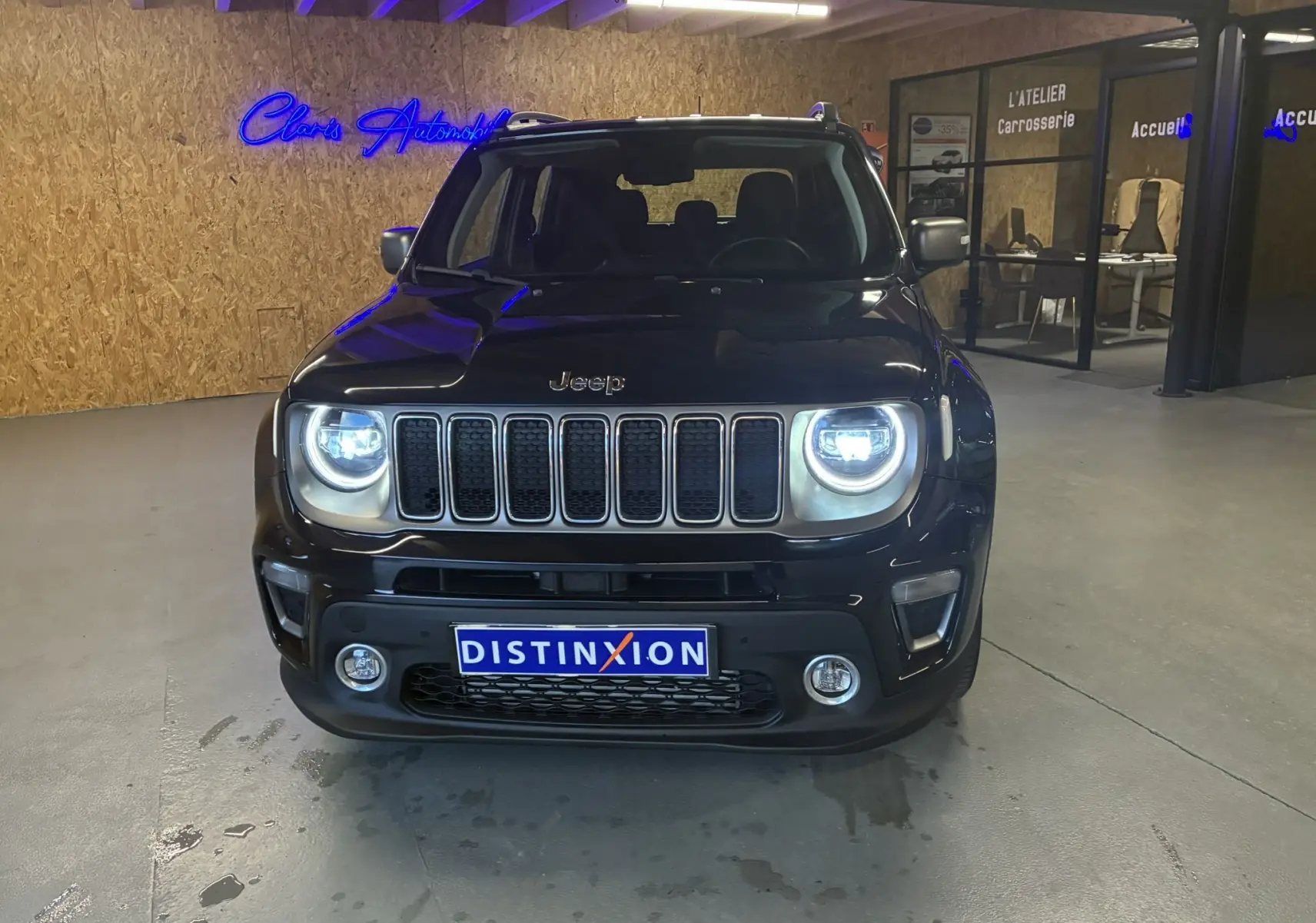 Vue de face d'un Jeep Renegade noir 2019 avec phares allumés dans un garage au sol béton.
