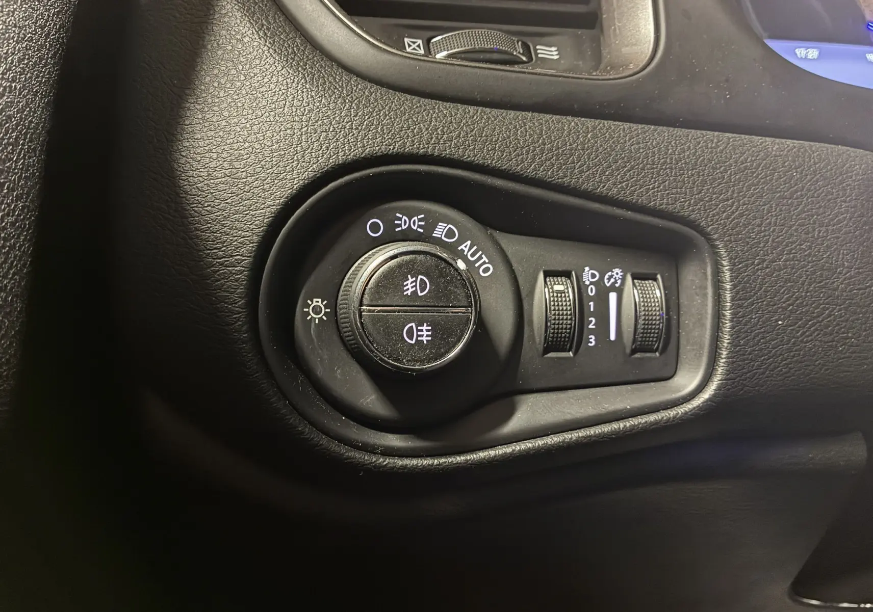 Gros plan sur le bouton de commande des phares du Jeep Renegade noir, avec réglages automatiques et variateurs d'intensité.