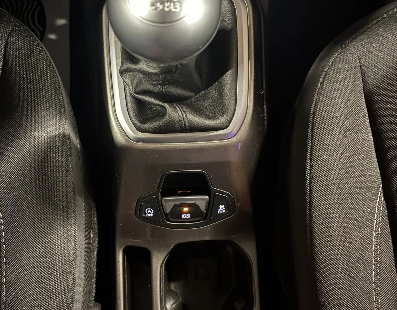 Vue plongeante sur la console centrale noire d'un Jeep Renegade 2019, mettant en valeur le levier de vitesse manuel et les commandes électroniques.