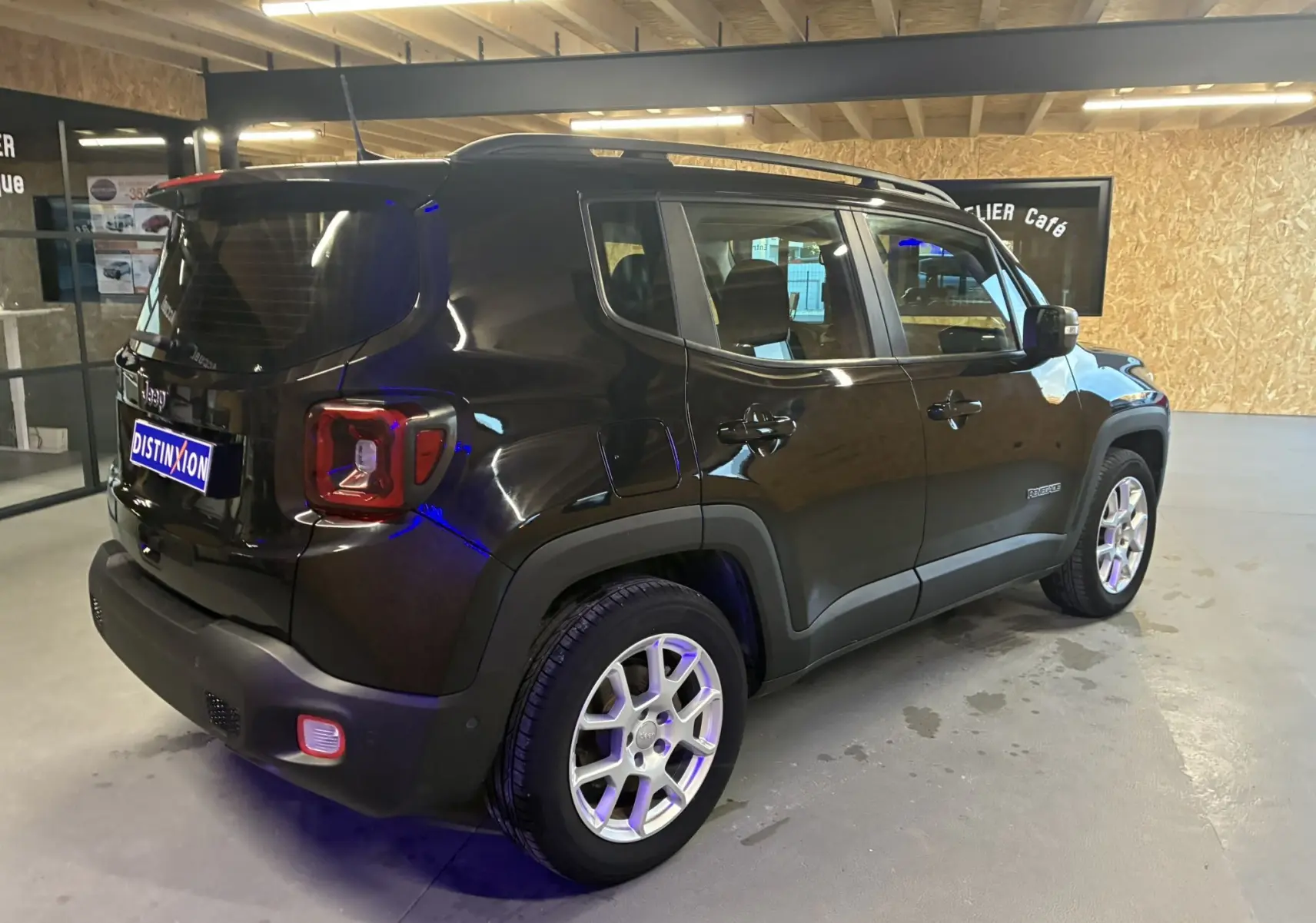 Jeep Renegade noir vu en 3/4 arrière droit dans un garage, avec jantes argentées et feux arrière carrés rouges.