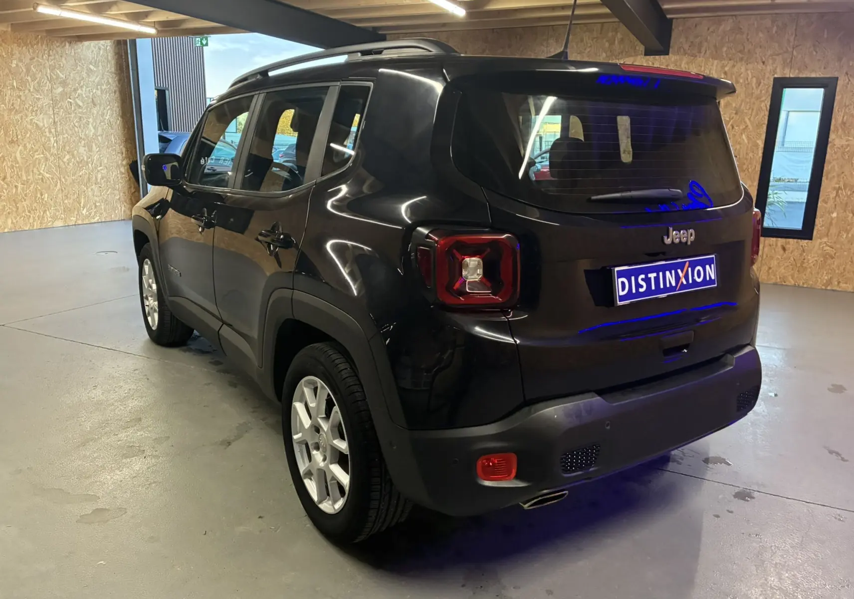 Jeep Renegade noir vue 3/4 arrière droit dans un garage, mettant en valeur ses feux arrière carrés et ses jantes argentées.