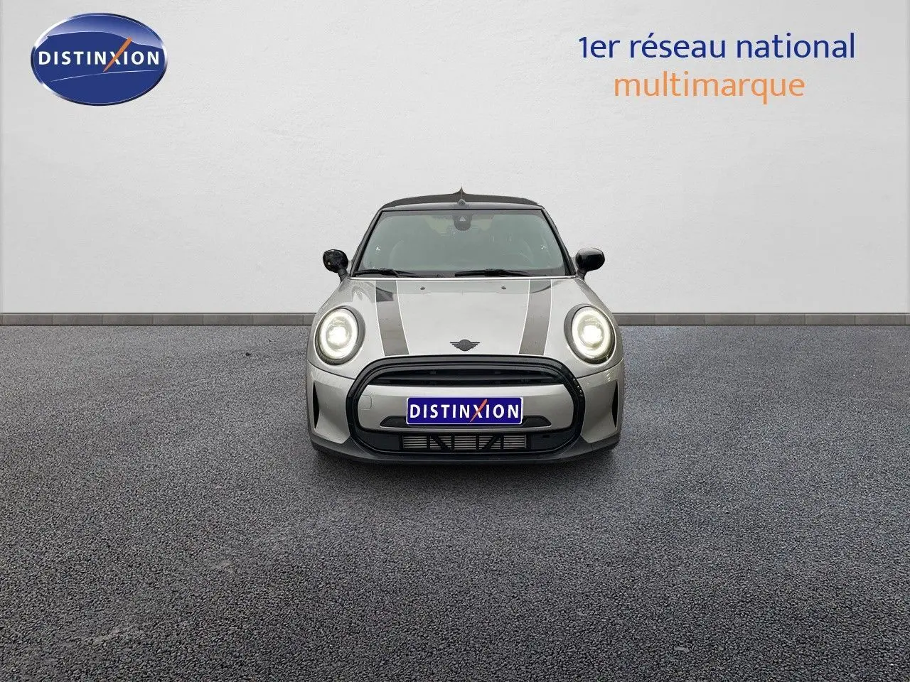 Vue frontale d'une MINI Cabriolet 2023 couleur Melting Silver Metal avec phares allumés et bandes noires sur le capot.