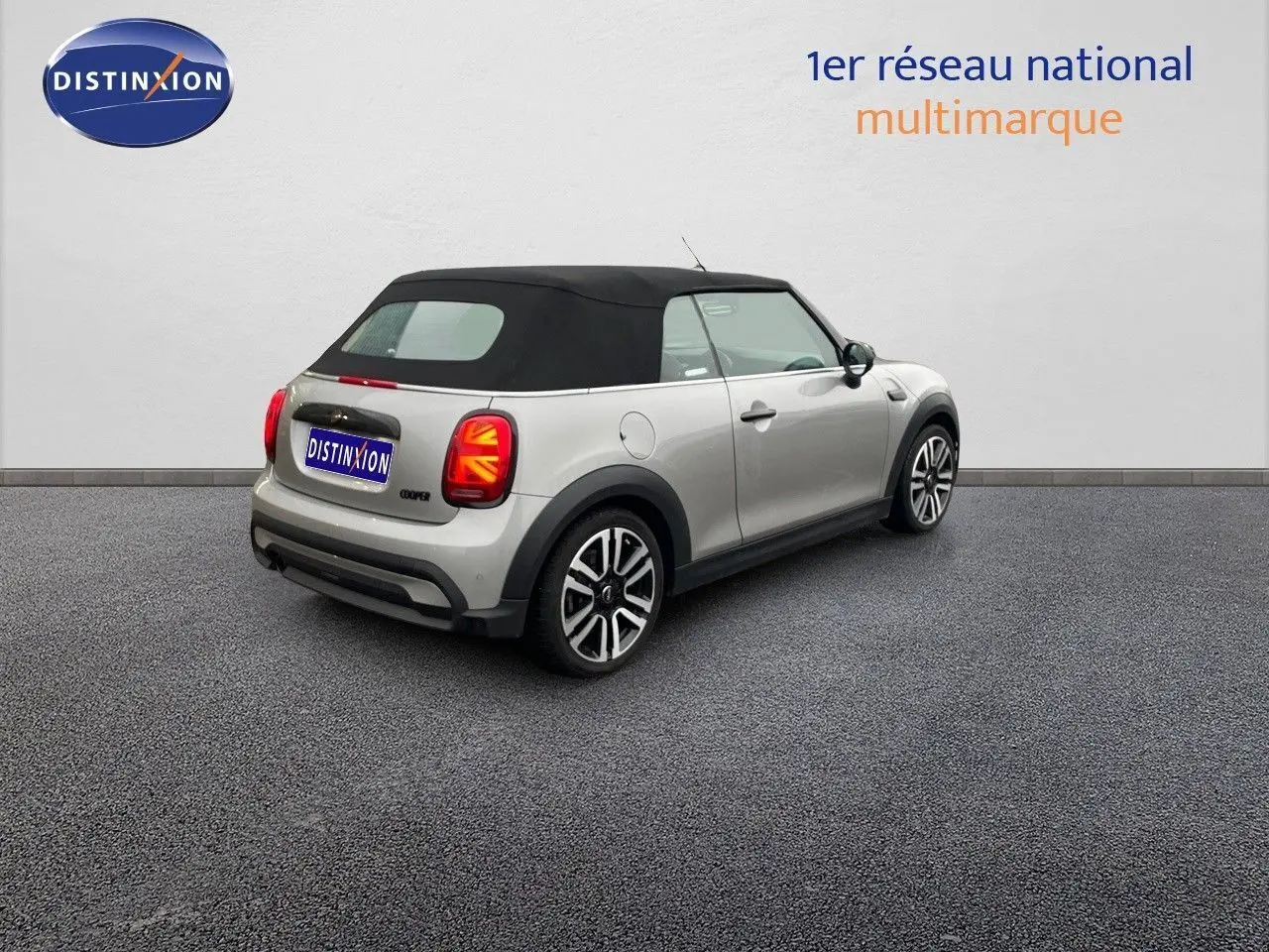 Vue 3/4 arrière droite d'une MINI Cabriolet 2023 Melting Silver avec toit noir et feux arrière à motif Union Jack.