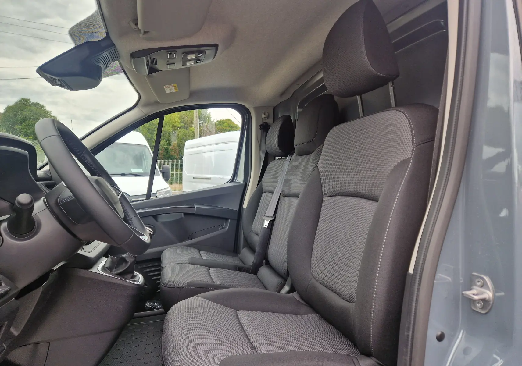 Vue intérieure côté conducteur du Renault Trafic Fourgon gris urbain 2025, montrant les sièges tissu et le volant.