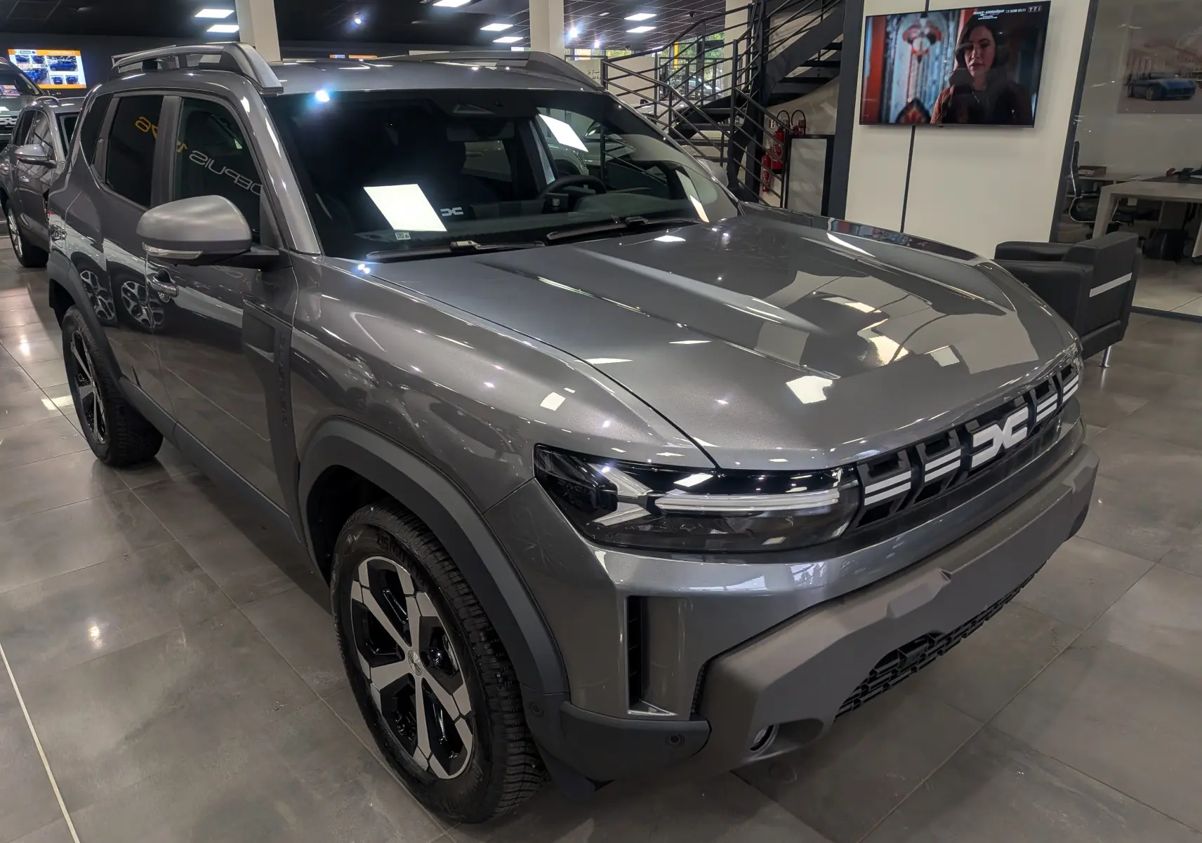 Dacia Duster gris schiste en 3/4 avant droit, avec calandre moderne et jantes noires bicolores en showroom.