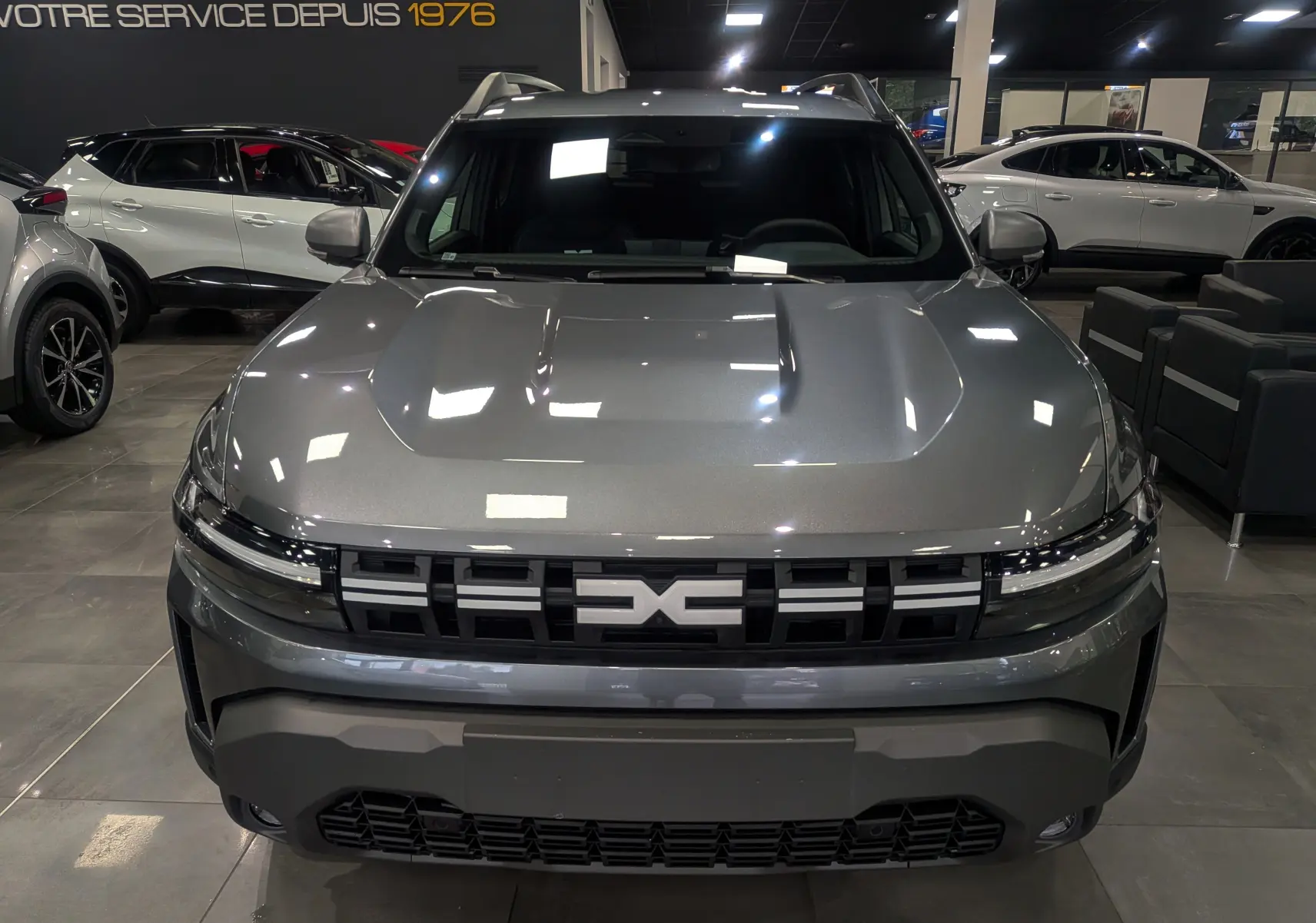 Vue de face du Dacia Duster 2025 gris schiste avec sa calandre distinctive et ses phares fins en showroom.