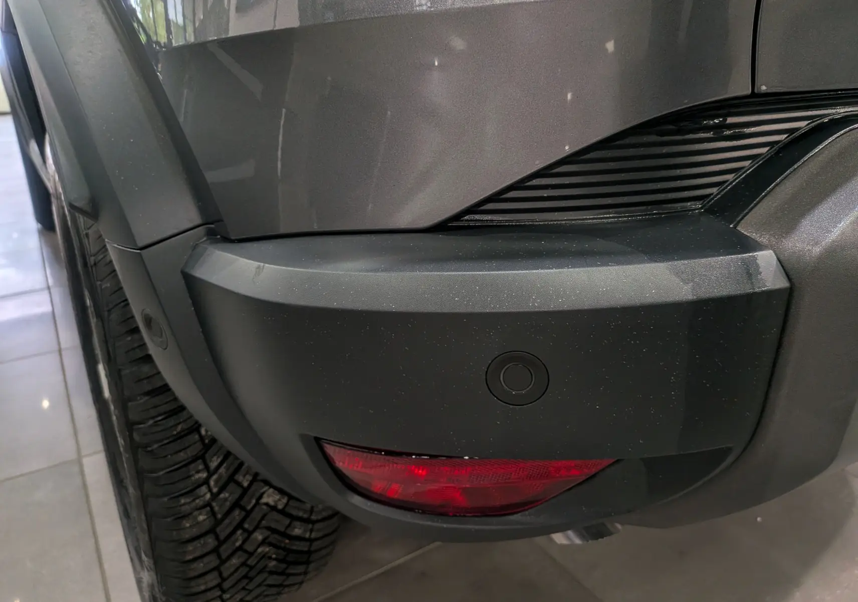Gros plan sur le pare-chocs arrière droit gris schiste du Dacia Duster 2025 avec feu antibrouillard et capteur de recul.