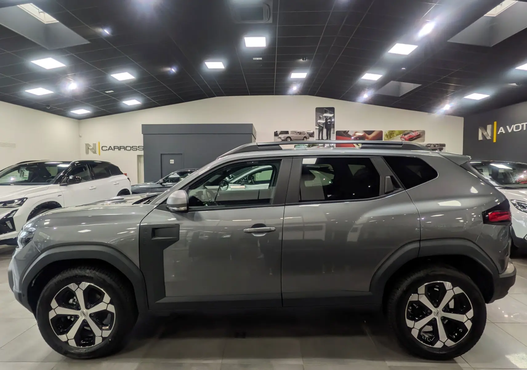 Profil côté gauche du Dacia Duster gris schiste 2025 en version Mild Hybrid 130 CH 4x4 JOURNEY, en showroom lumineux.