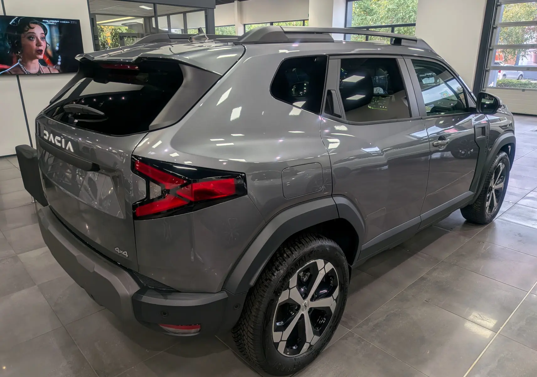Vue 3/4 arrière droite du Dacia Duster gris schiste avec jantes bi-ton et logo 4x4 visible en showroom.