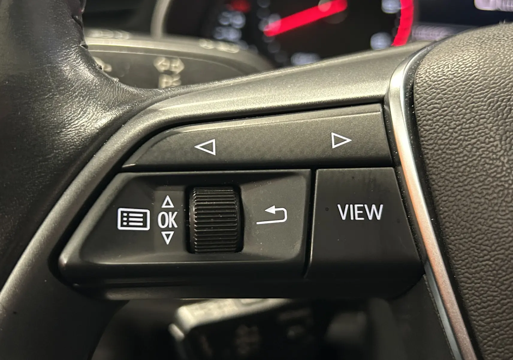 Gros plan sur les commandes gauche du volant en cuir noir de l'Audi A6 Avant 2019, boutons de navigation et fonction View visibles.