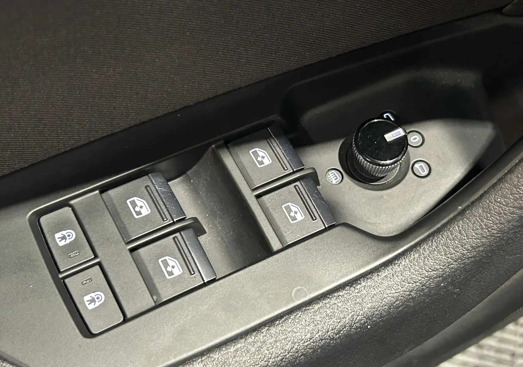 Gros plan sur les commandes de lève-vitres et réglage des rétroviseurs côté conducteur d'une Audi A6 Avant noire 2019.