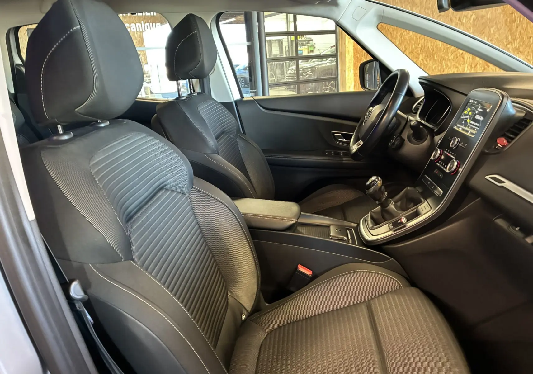 Vue intérieure côté conducteur du Renault Grand Scenic gris 2017, sièges noirs, tableau de bord avec écran tactile et boîte manuelle.