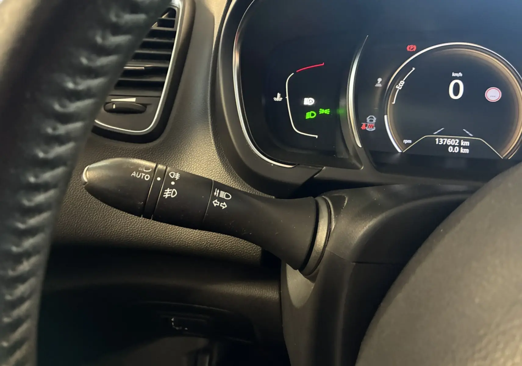 Gros plan sur la manette des feux et le tableau de bord numérique noir du Renault Grand Scenic gris 2017, côté gauche du volant.