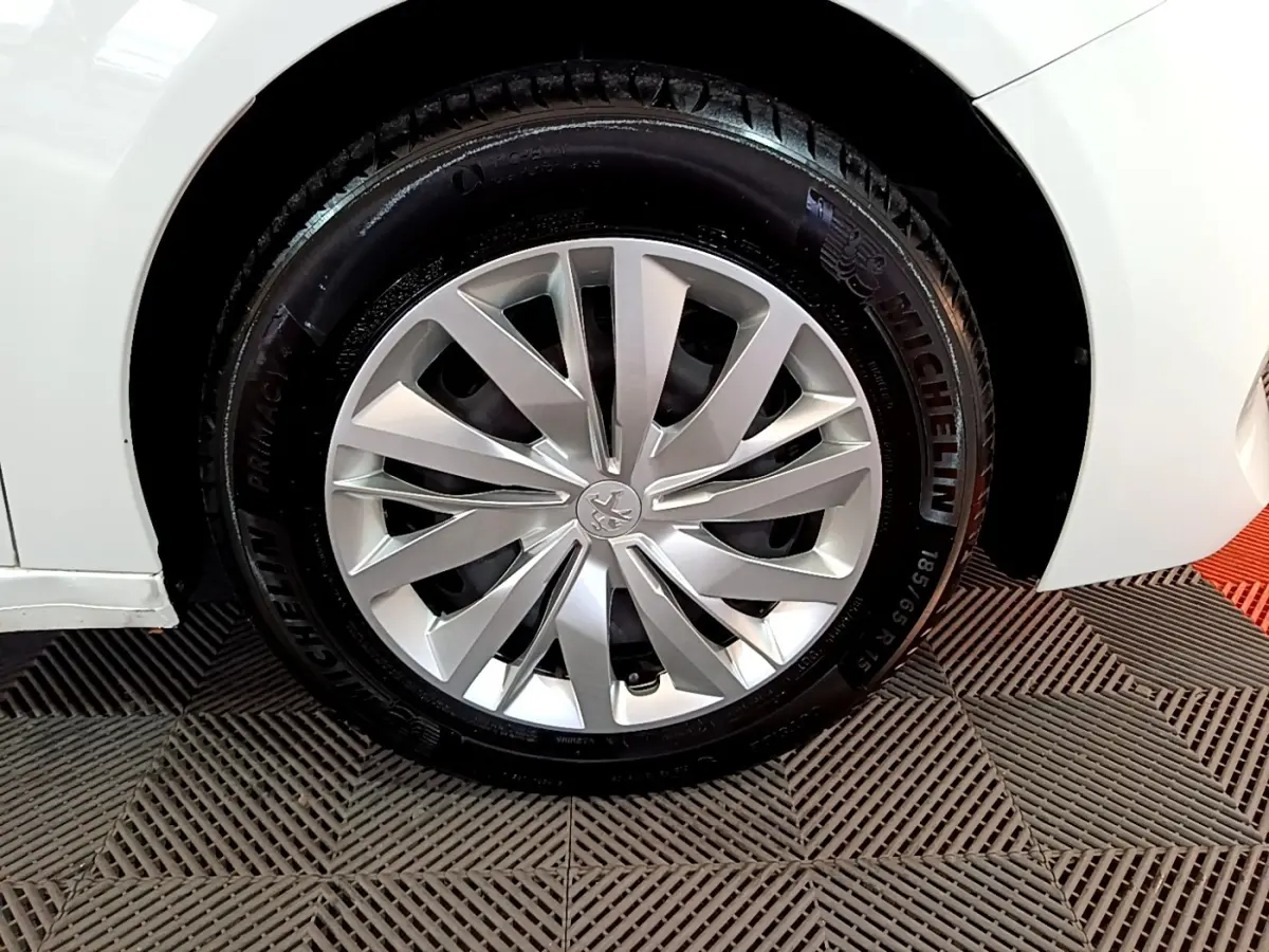 Gros plan sur la roue avant droite d'une Peugeot 208 blanche, mettant en valeur la jante alliage et le pneu Michelin.