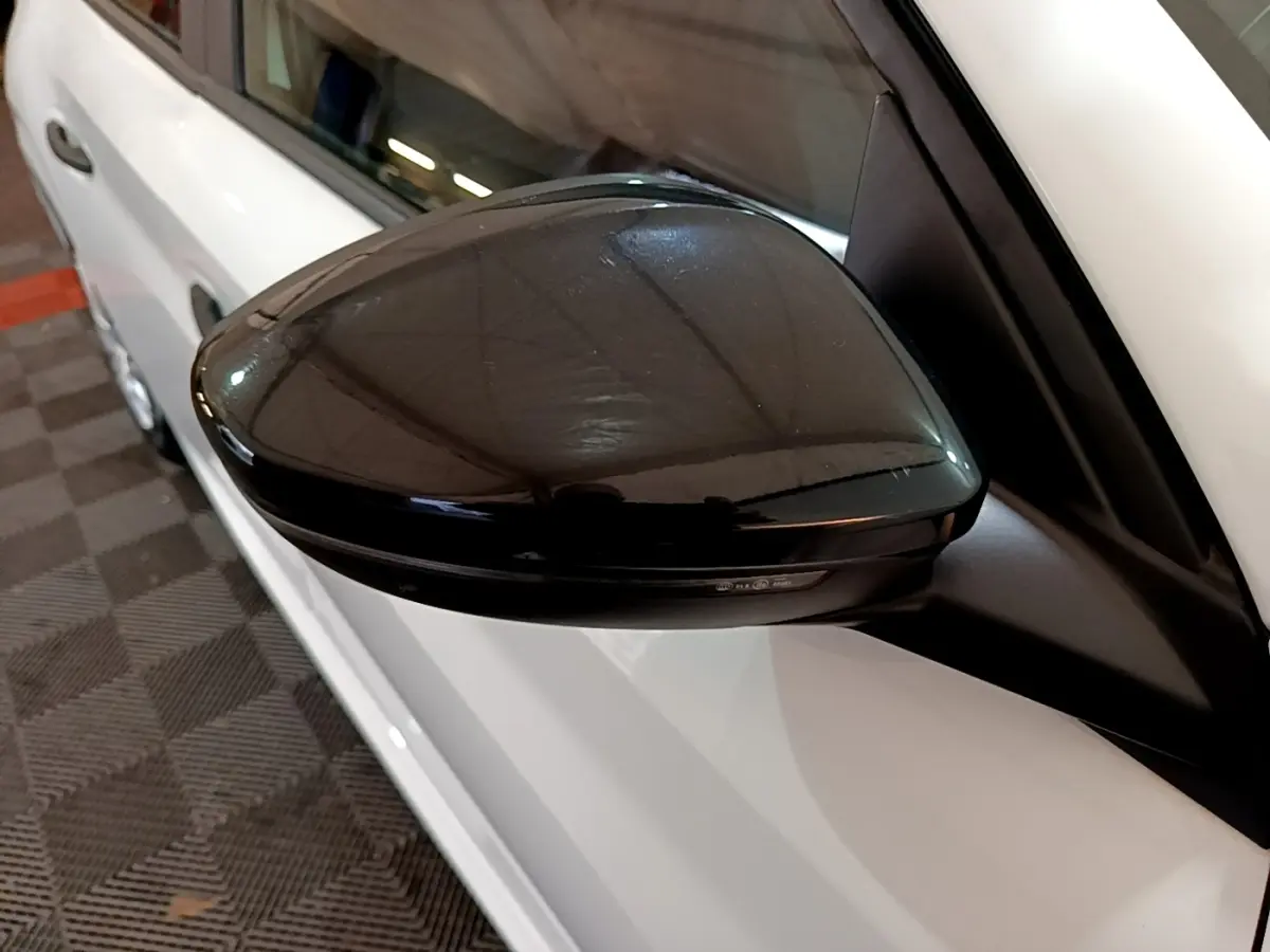 Rétroviseur noir en gros plan côté gauche d'une Peugeot 208 blanche, vue partielle du véhicule stationné.