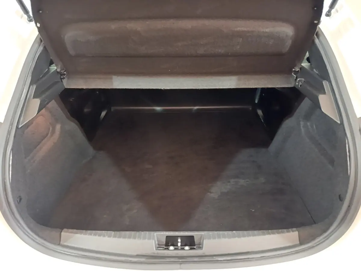 Coffre ouvert vu de l'arrière d'une Peugeot 208 blanche, montrant un espace de chargement vide et propre.