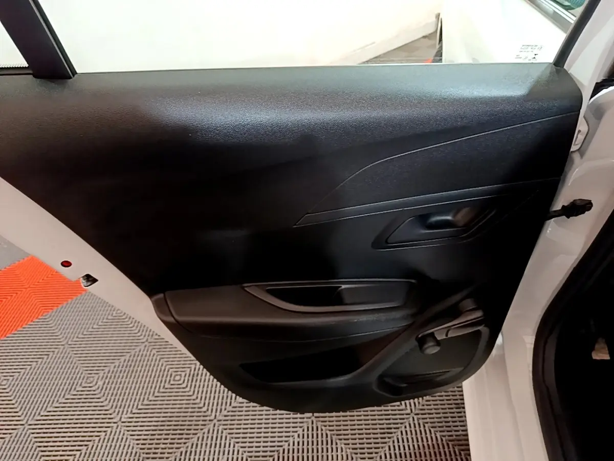 Vue rapprochée de la porte arrière droite noire d'une Peugeot 208 blanche de 2022, avec poignée intérieure visible.