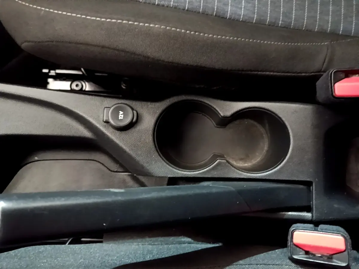 Vue rapprochée de la console centrale noire avec porte-gobelets et prise 12V dans une Peugeot 208 blanche.