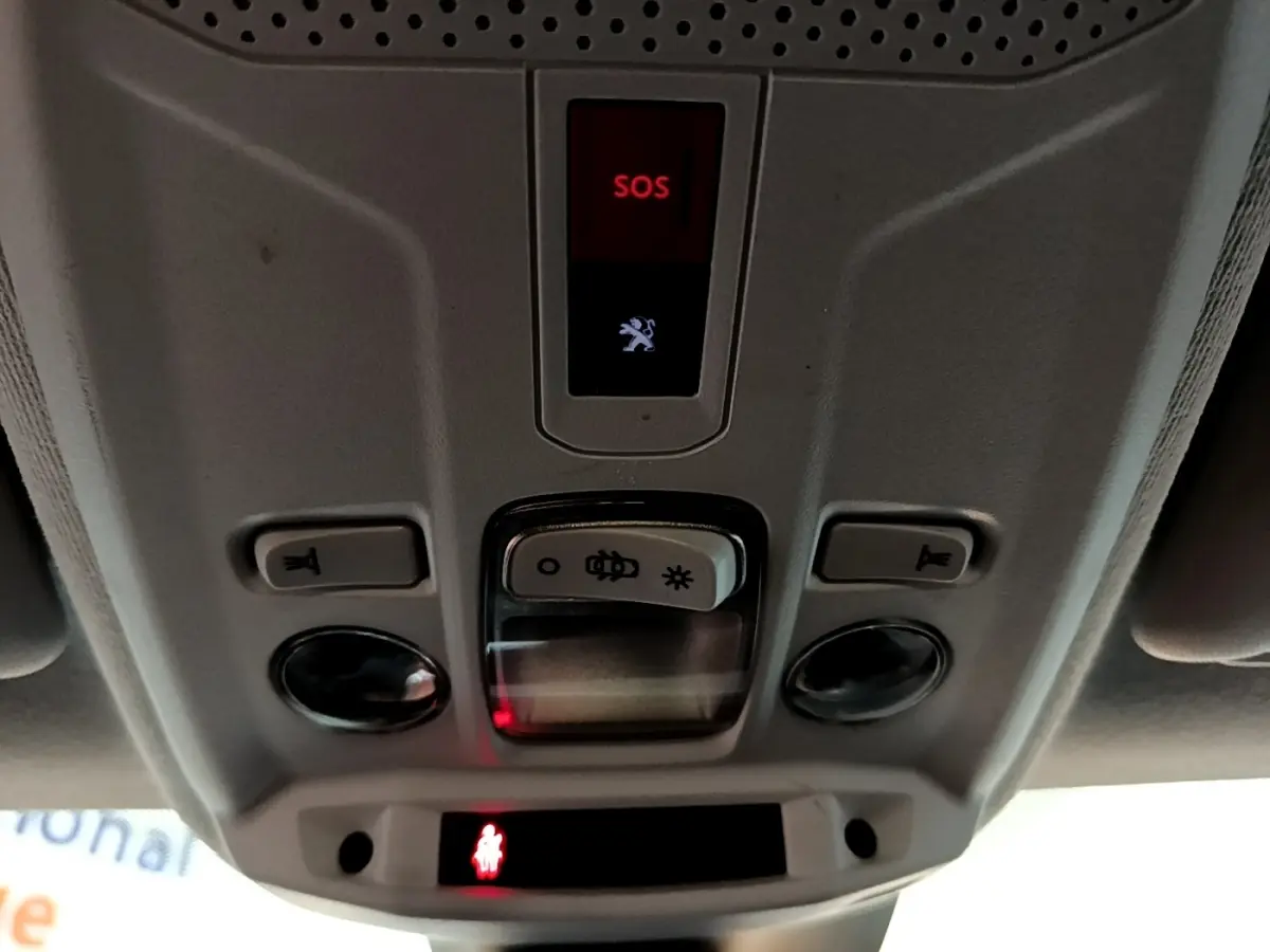 Vue en contre-plongée du panneau de commandes plafond gris clair de la Peugeot 208 blanc, avec bouton SOS rouge allumé.