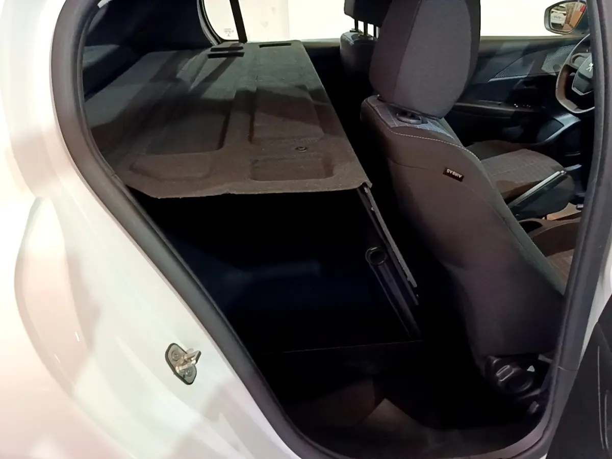 Vue intérieure côté arrière droit du coffre ouvert d'une Peugeot 208 blanche avec banquette rabattue et sièges tissu gris.