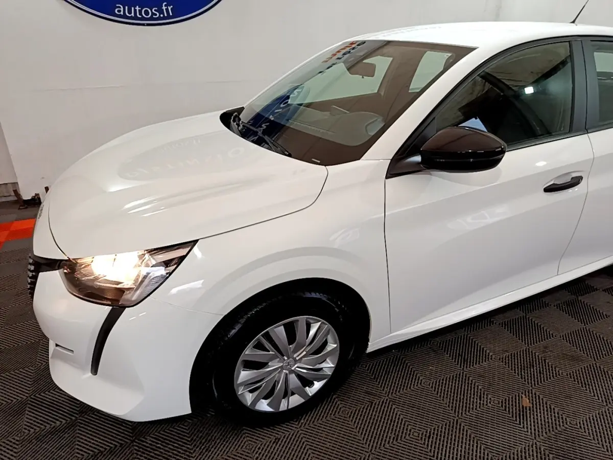 Vue 3/4 avant droit d'une Peugeot 208 blanche avec phares allumés et rétroviseur noir brillant.