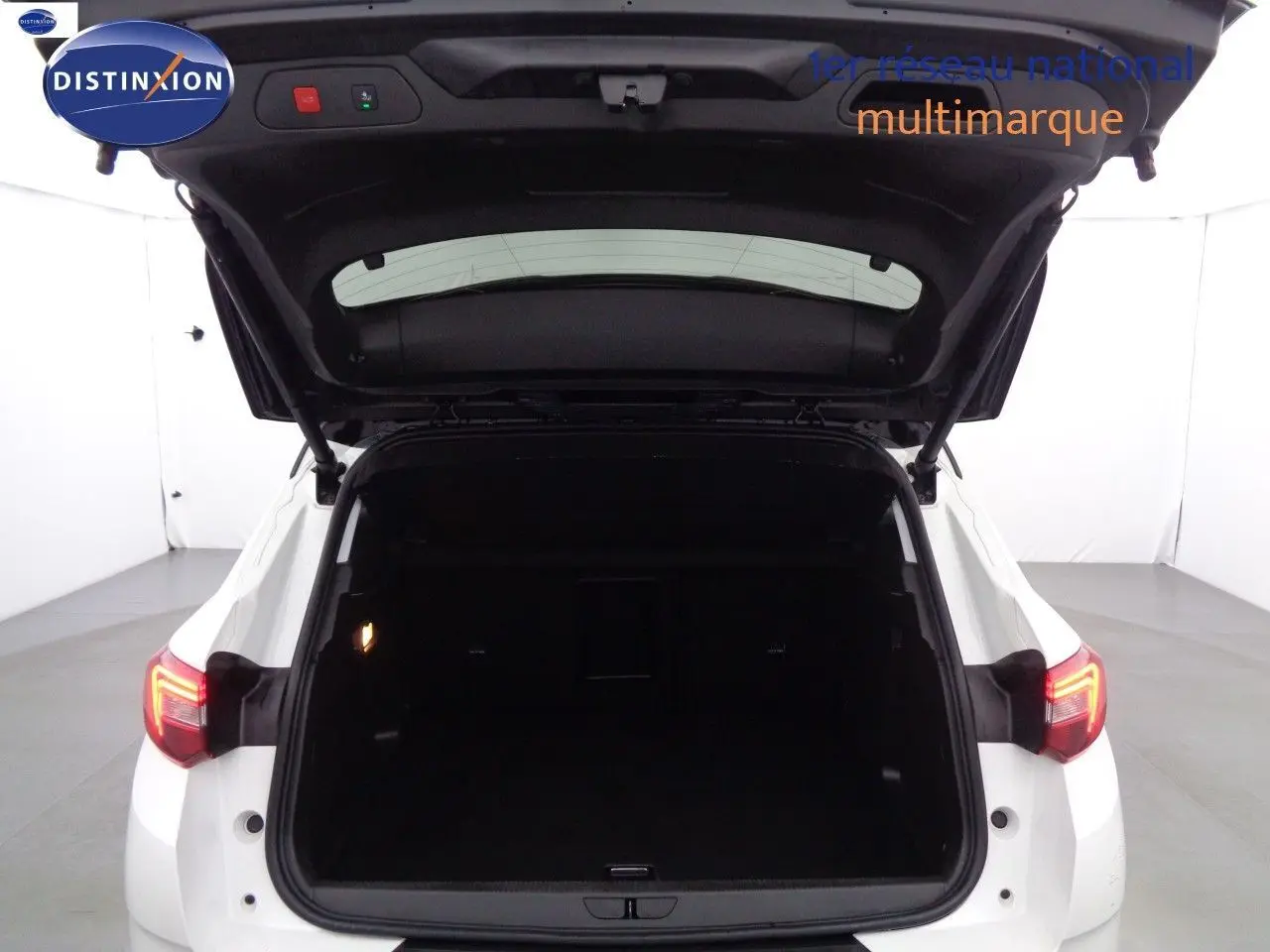 Vue arrière du coffre ouvert d'un Opel Grandland X blanc nacré, avec feux arrière allumés dans un studio lumineux.