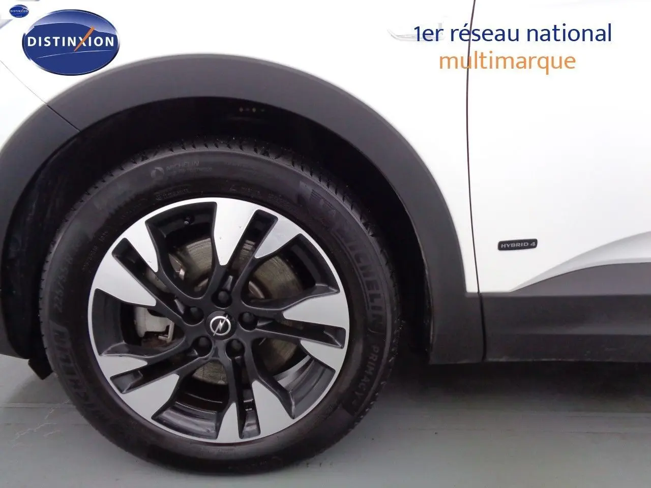 Gros plan sur la roue avant gauche d'un Opel Grandland X blanc nacré avec jante alliage bicolore et badge Hybrid 4.