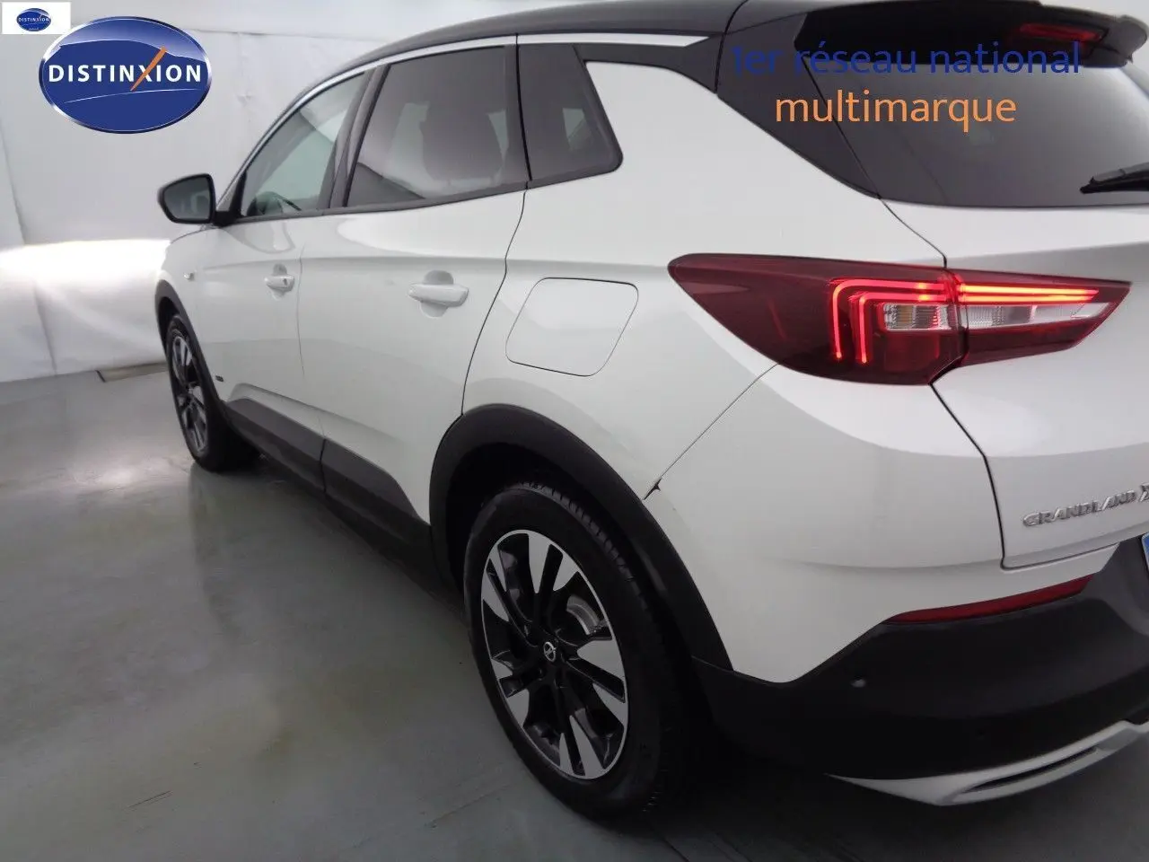 Vue 3/4 arrière droite d'un Opel Grandland X blanc nacré avec feux arrière LED et jantes noires bicolores.