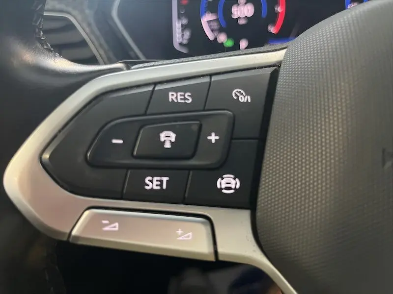 Gros plan sur les commandes du volant côté gauche du Volkswagen T-Cross gris Limestone, avec régulateur de vitesse adaptatif.