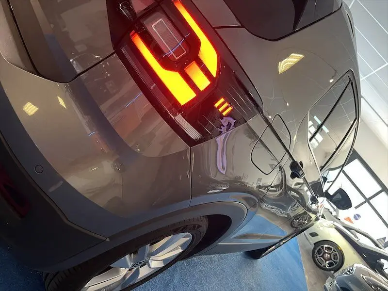 Vue 3/4 arrière droite d'un Volkswagen T-Cross gris Limestone métallisé avec feux arrière allumés en intérieur showroom.