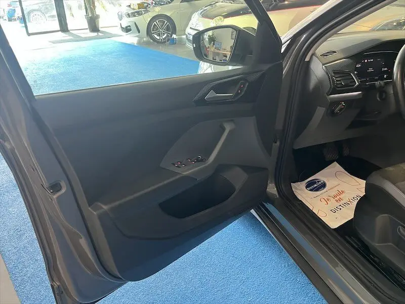 Vue intérieure côté conducteur d'un Volkswagen T-Cross gris Limestone, montrant la portière ouverte et le tableau de bord.