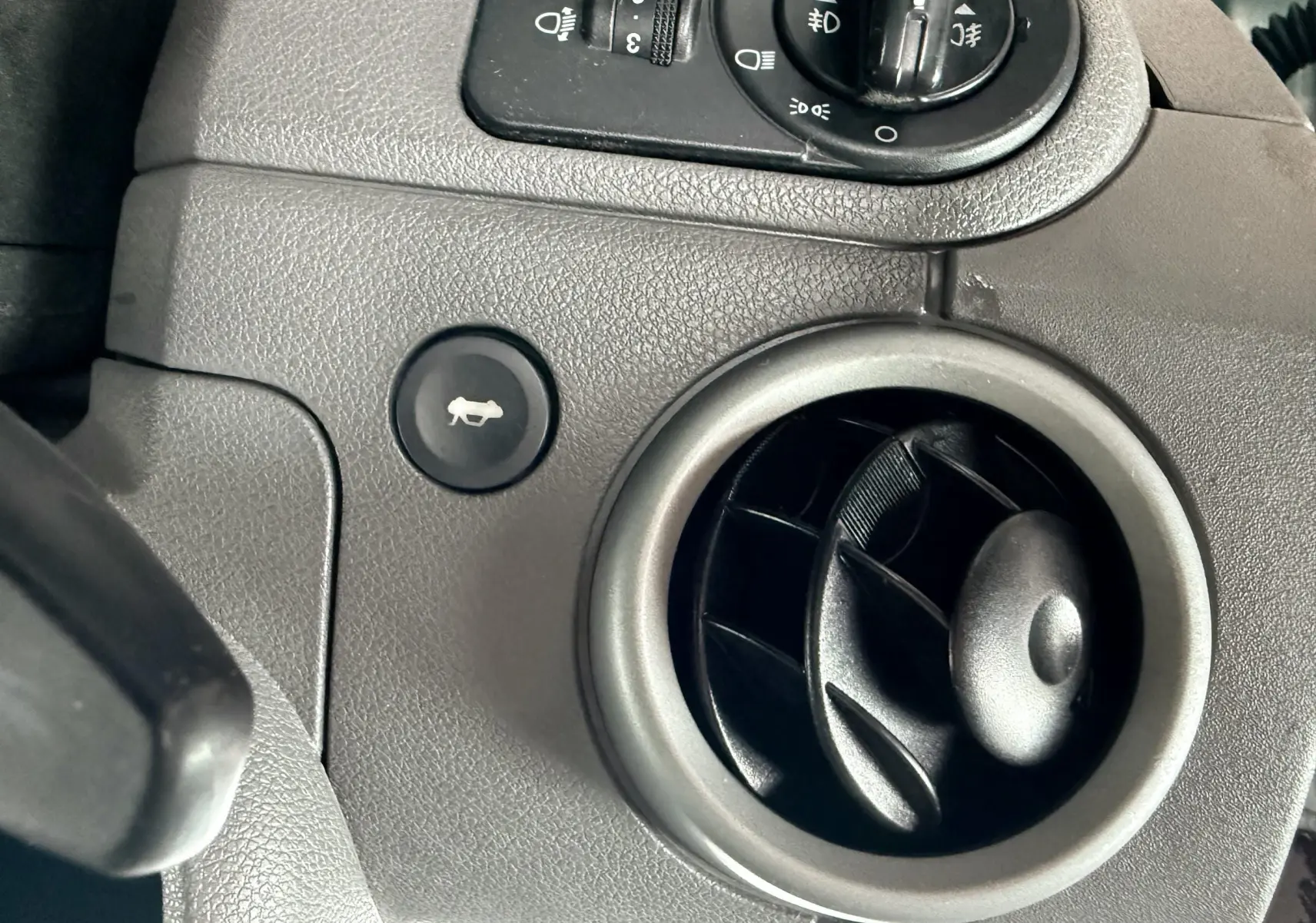 Gros plan sur la commande d'ouverture du capot et la sortie d'air ronde du tableau de bord gris foncé d'une Ford Fusion 2002.