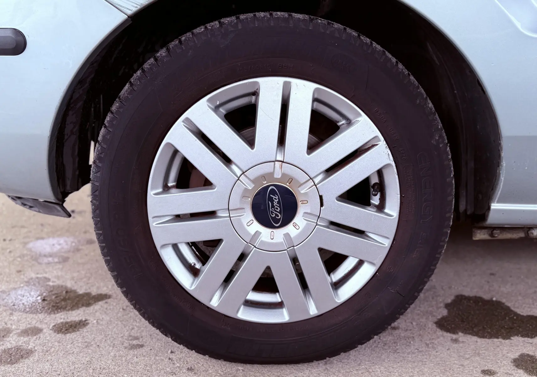 Gros plan sur la roue avant droite d'une Ford Fusion bleu clair de 2002 avec jante argentée et logo Ford au centre.