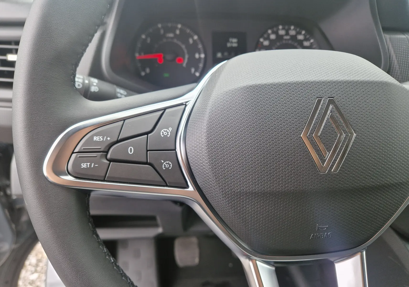 Gros plan sur le volant du Renault Trafic Fourgon gris urbain 2025, avec commandes intégrées et logo central brillant.