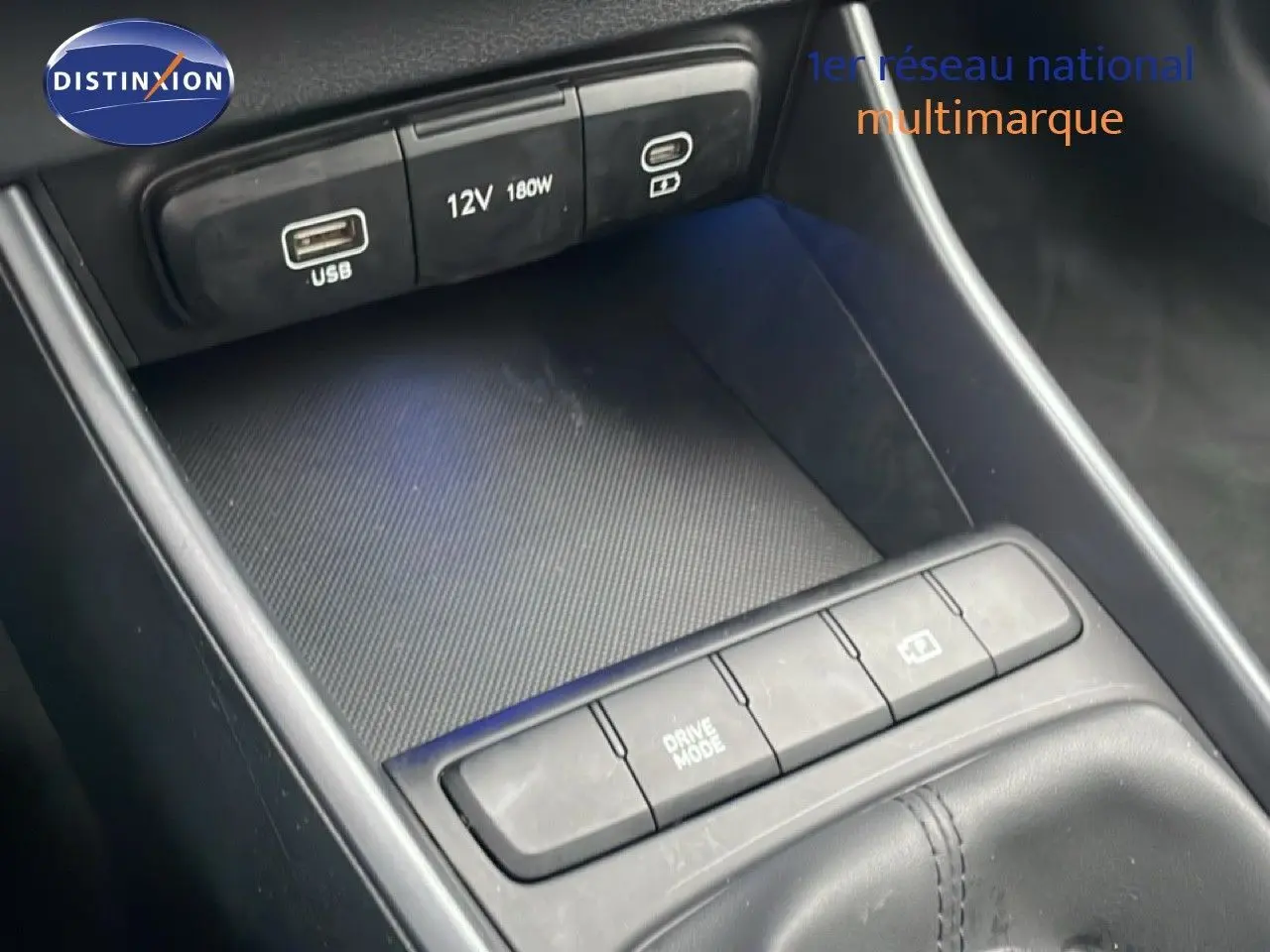 Gros plan sur la console centrale noire de la Hyundai i20 2025, montrant les ports USB, prise 12V et boutons de commande.