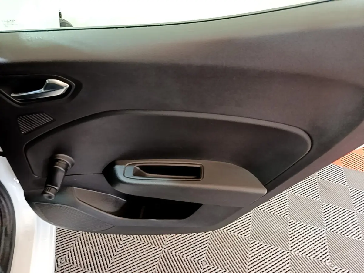 Vue intérieure sur la porte avant gauche noire d’une Renault Clio Business blanche, avec poignée et commande manuelle de vitre.