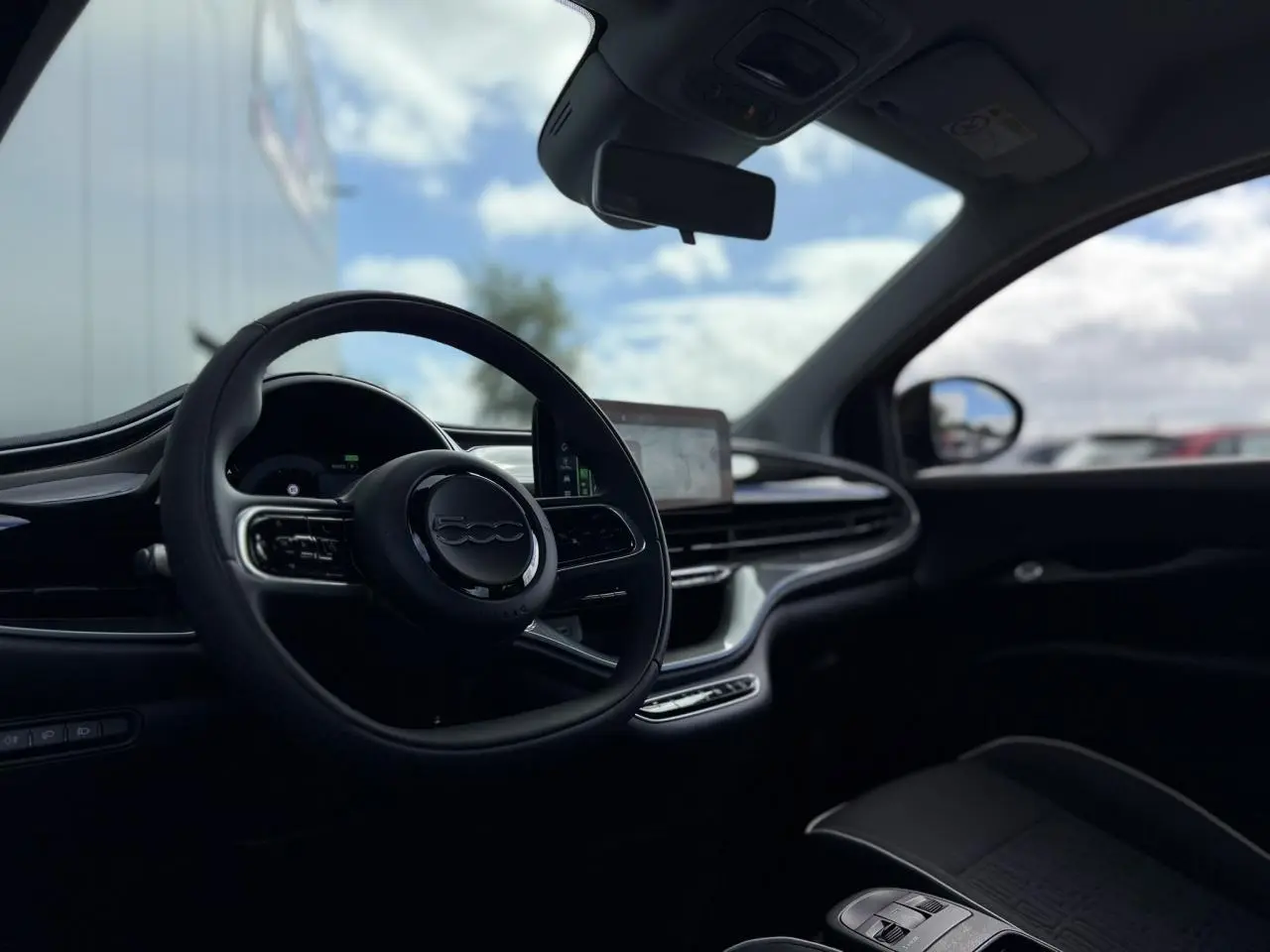 Vue intérieure côté conducteur de la Fiat 500 électrique 2024 en Noir Onyx, volant Soft-Touch et écran tactile central visible.