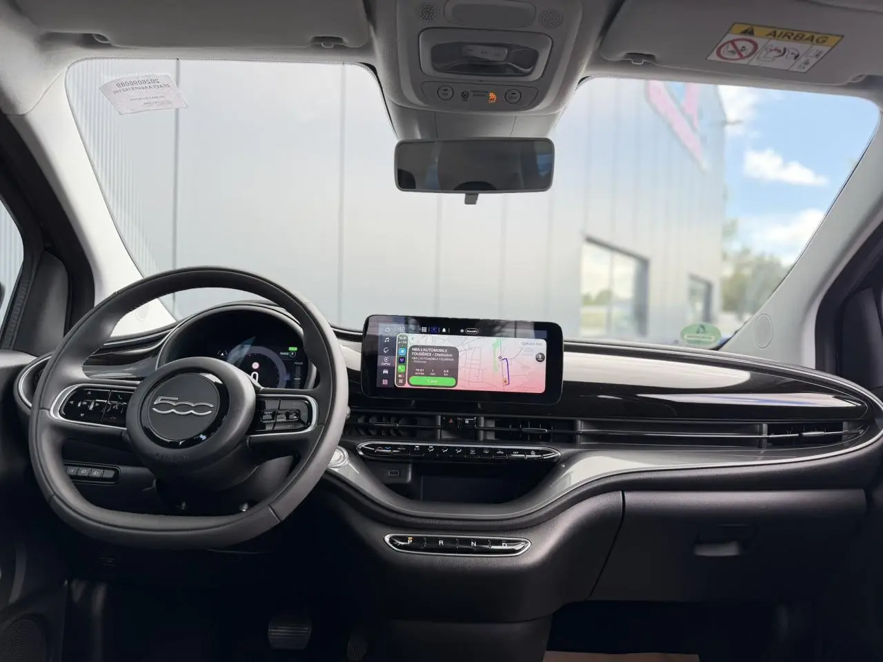 Vue frontale de l'habitacle du Fiat 500 électrique 2024, avec tableau de bord noir brillant et écran tactile central.