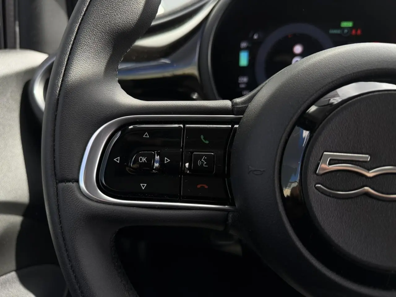 Gros plan sur le volant noir Soft-Touch du Fiat 500 électrique 2024 avec commandes intégrées et logo 500 au centre.