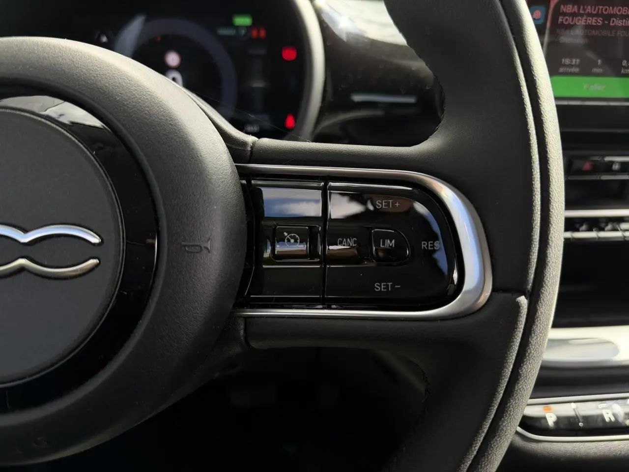 Gros plan sur le volant noir Soft-Touch de la Fiat 500 électrique 2024, avec commandes de régulateur de vitesse visibles.