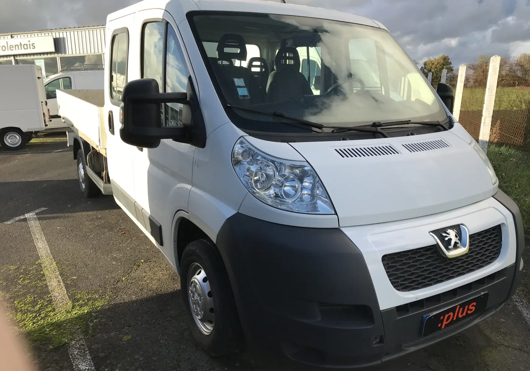 Vue 3/4 avant gauche d'un utilitaire blanc Peugeot Boxer Chassis Double Cabine avec plateau et sept places visibles.